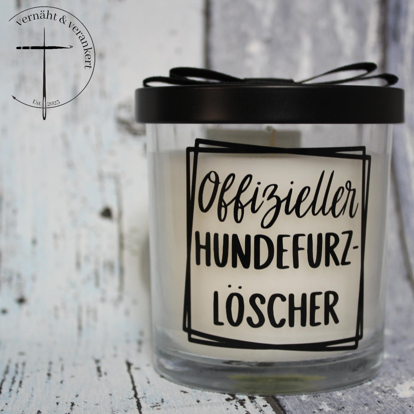 Eine Duftkerze mit einem Deckel, welcher auf Glas ist. Auf dem Glas steht "Offizieller Hundefurzlöscher".