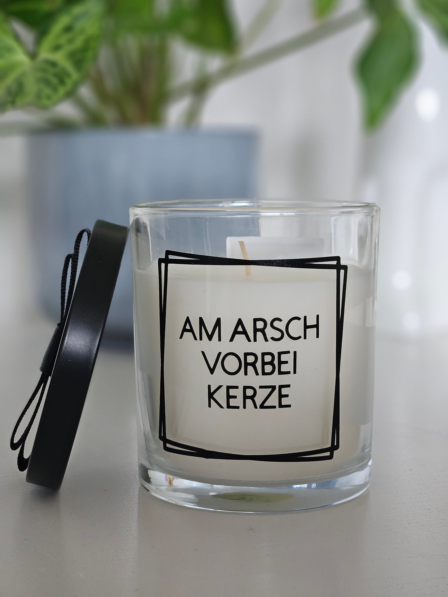 Eine Duftkerze mit Deckel und einem witzigen Spruch auf dem Glas, von vorne fotografiert