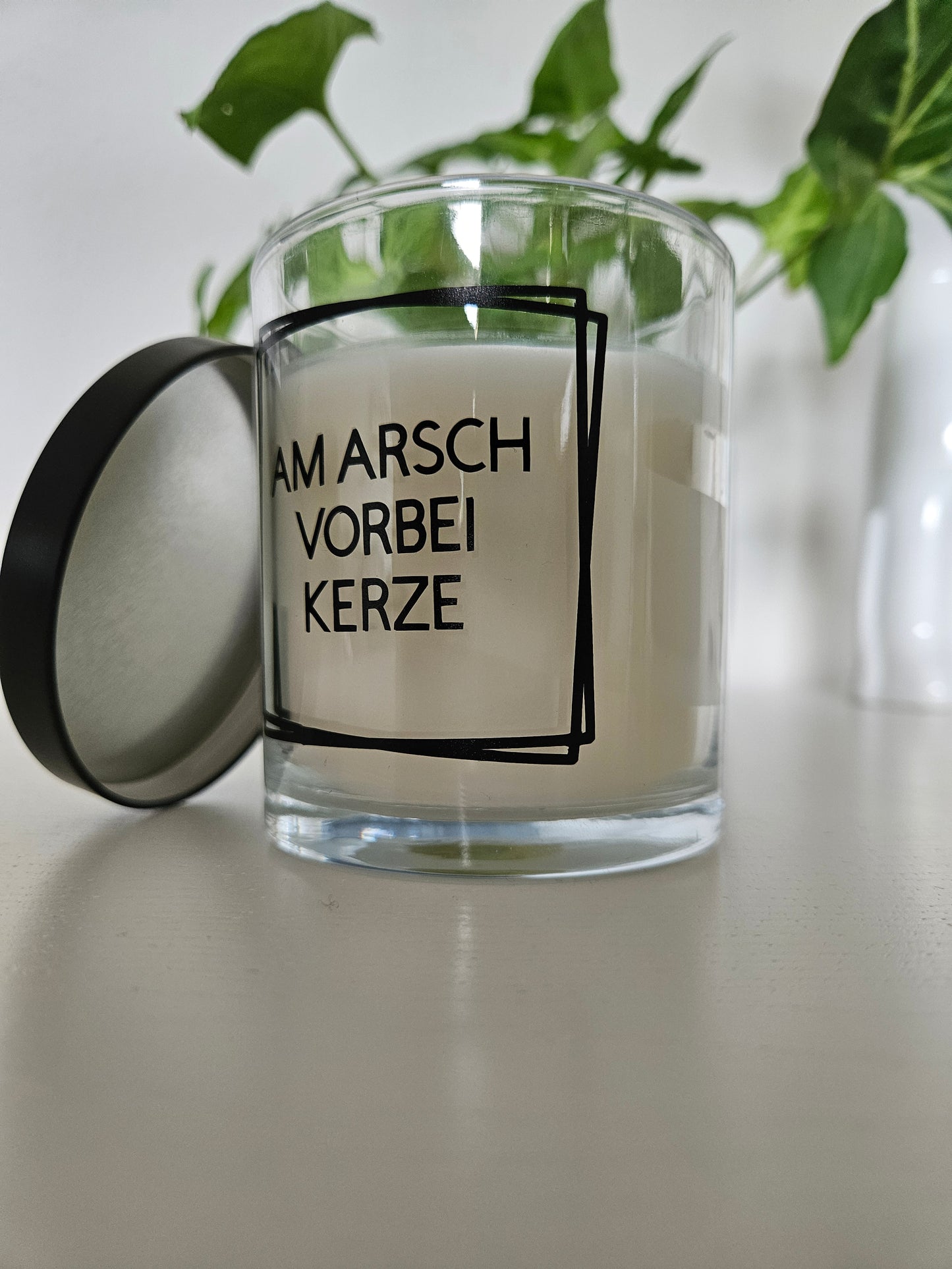 Eine Duftkerze mit Deckel und einem witzigen Spruch auf dem Glas, von unten fotografiert