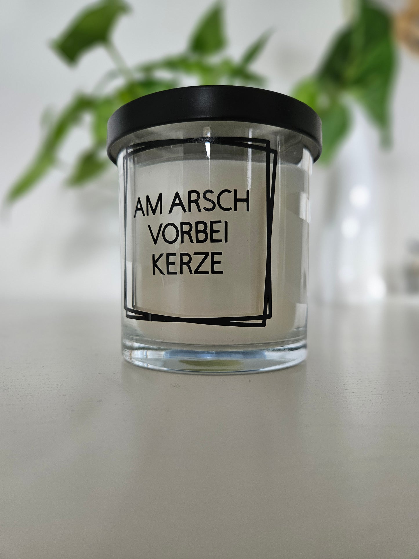 Eine Duftkerze mit Deckel und einem witzigen Spruch auf dem Glas, von rechts fotografiert