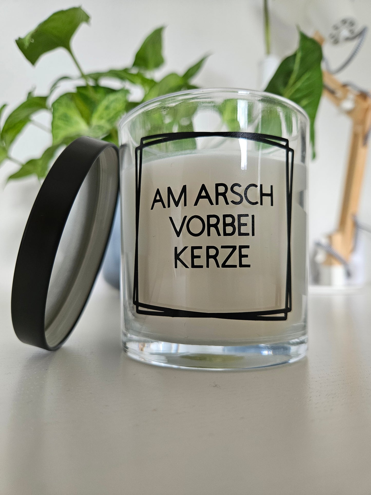 Eine Duftkerze mit Deckel und einem witzigen Spruch auf dem Glas, von links fotografiert