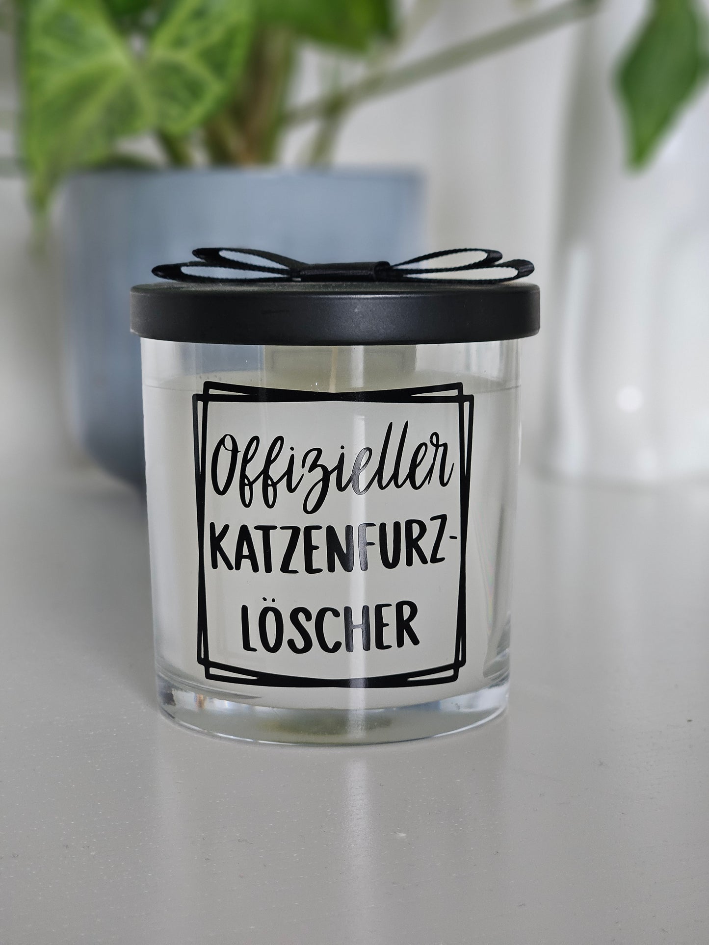 Eine Duftkerze von vorne Fotografiert, mit der Aufschrift, Offizieller Katzenfurzlöscher. Das Glas ist geschlossen und der Deckel ist auf dem Glas.