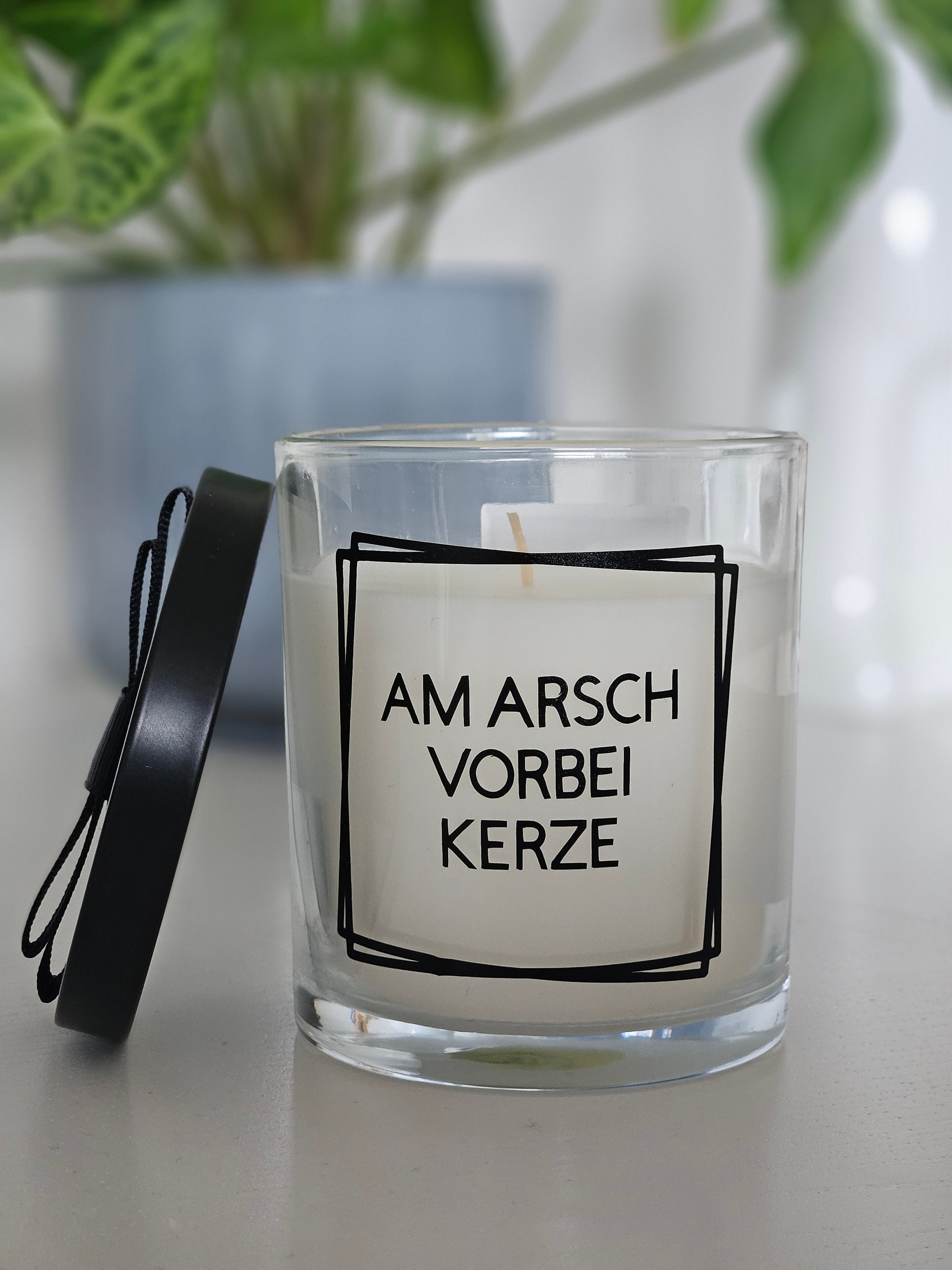 Eine Duftkerze mit Deckel und einem witzigen Spruch auf dem Glas, von vorne fotografiert