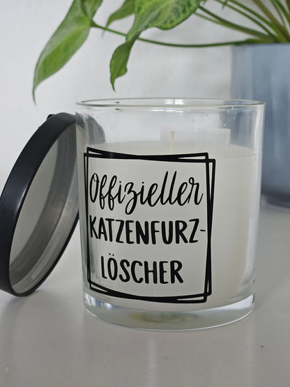 Eine Duftkerze von der Seite fotografiert, mit der Aufschrift, Offizieller Katzenfurzlöscher. Das Glas ist offen und der Deckel ist angelehnt